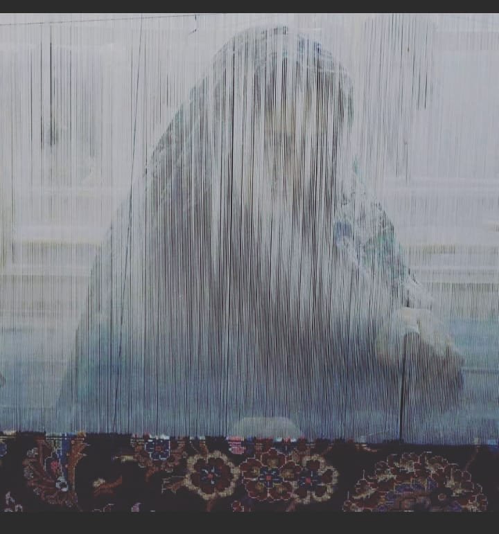 A weaver at the loom crafting a hand-knotted rug